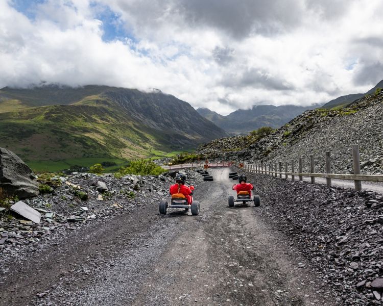 two people on the dirt track at zip world quarry karts with mountains in the background