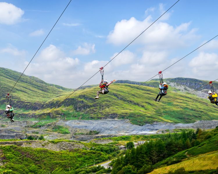 view of people going down the zip lines at zip world titan in wales with mountains in the background