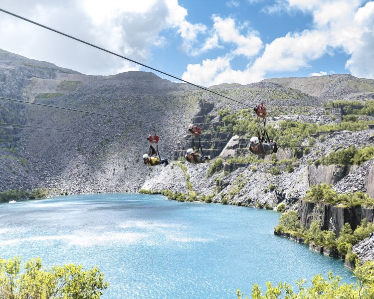 people on the zip lines going over the quarry lake at zip world velocity in wales