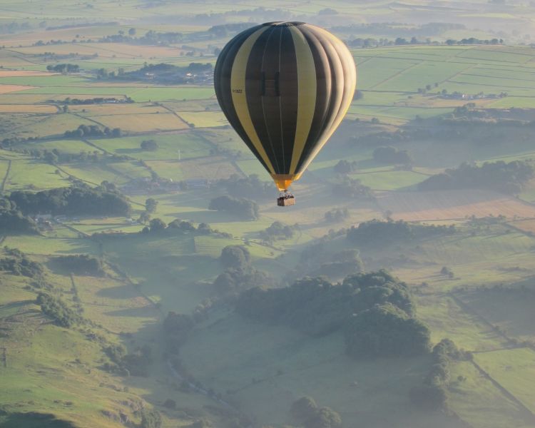 a striped hot air balloon balloon flying over countryside of rolling hills