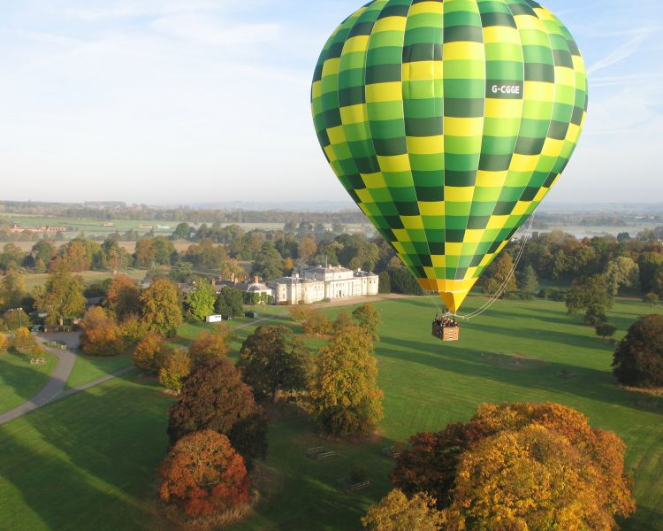 a green and yellow hot air balloon flying over a mansion and its gardens