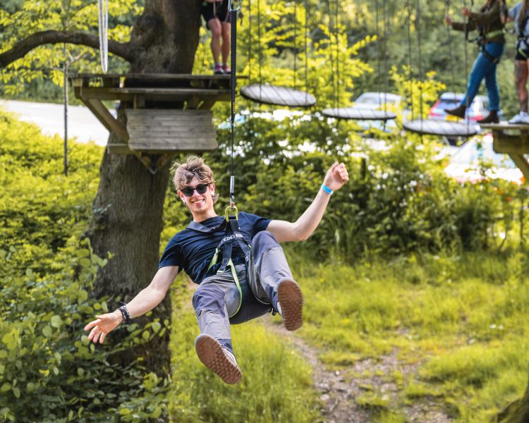 man hanging on the zip line on the zip world full trek manchester treetop obstacle course