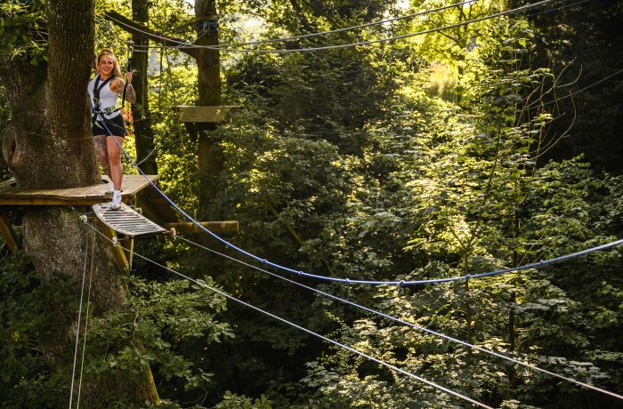 woman about to cross an obstacle on the zip world full trek manchester treetop obstacle course