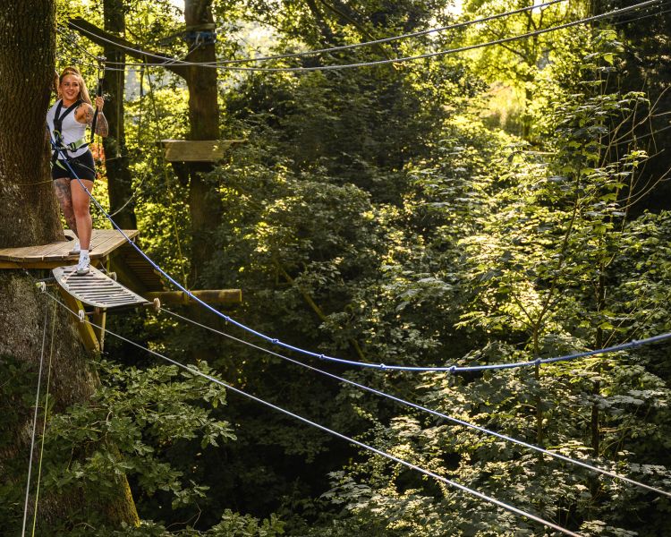 woman about to cross an obstacle on the zip world full trek manchester treetop obstacle course