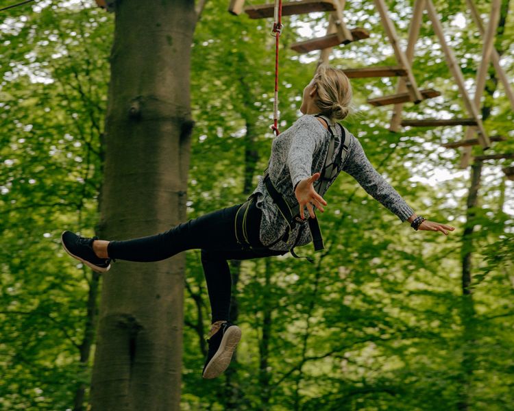 woman hanging from the zip world full trek manchester treetop obstacle course