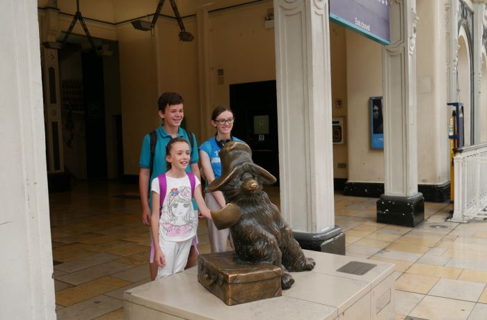 Three children having photo taken next to bronze statue of paddington on a walking tour in london