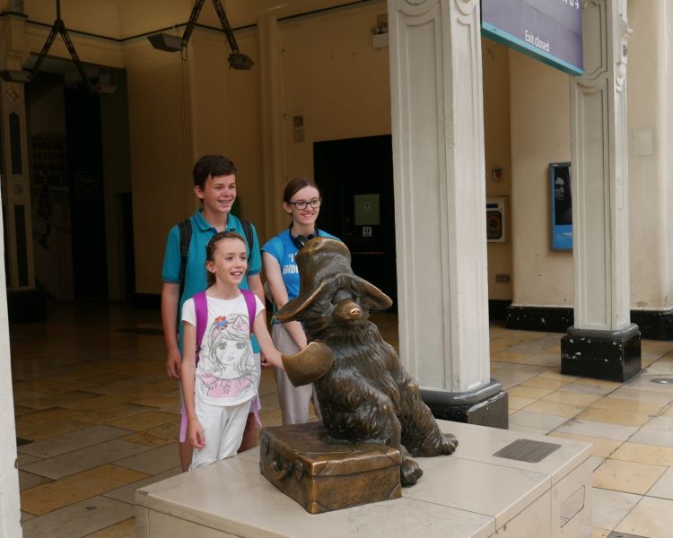 Three children having photo taken next to bronze statue of paddington on a walking tour in london