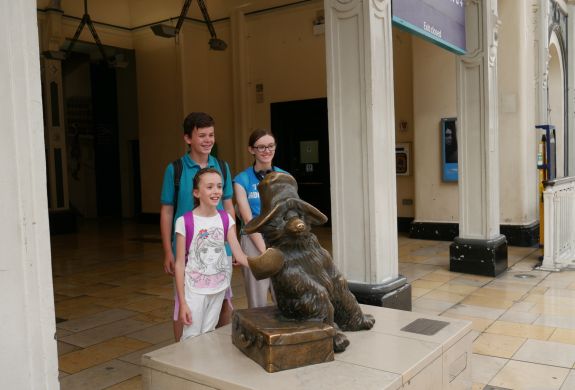 Three children having photo taken next to bronze statue of paddington on a walking tour in london