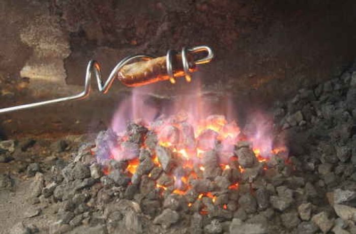 sausage being cooked over a fire using a sausage sizzler made on a blacksmith experience