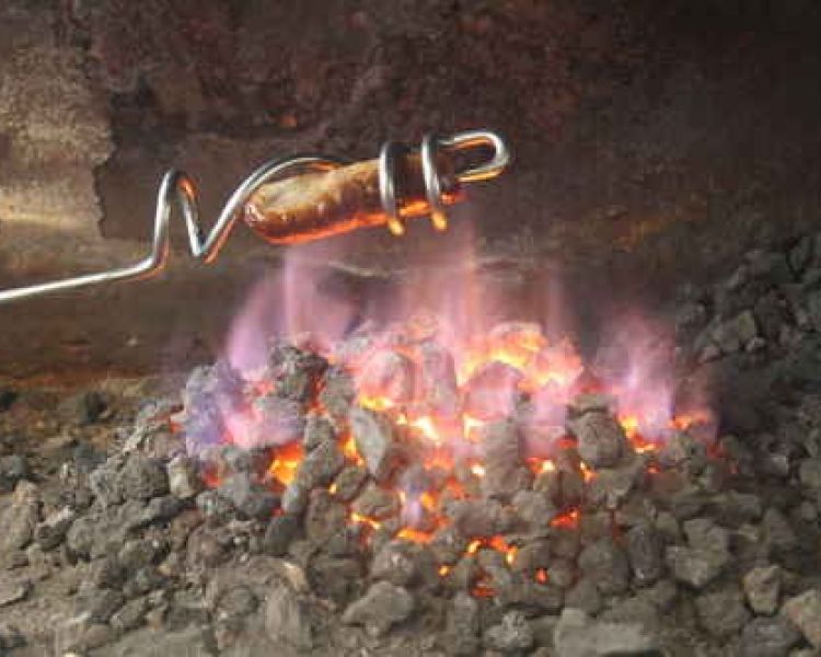 sausage being cooked over a fire using a sausage sizzler made on a blacksmith experience