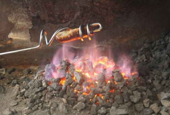 sausage being cooked over a fire using a sausage sizzler made on a blacksmith experience