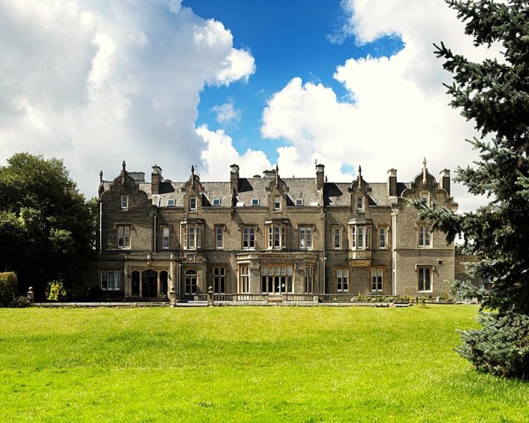 a view of the outside of shendish manor with a green lawn in the foreground and trees around the building