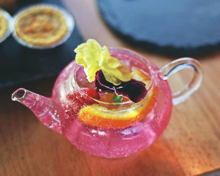 a glass teapot filled with pink gin and fruit and flowers