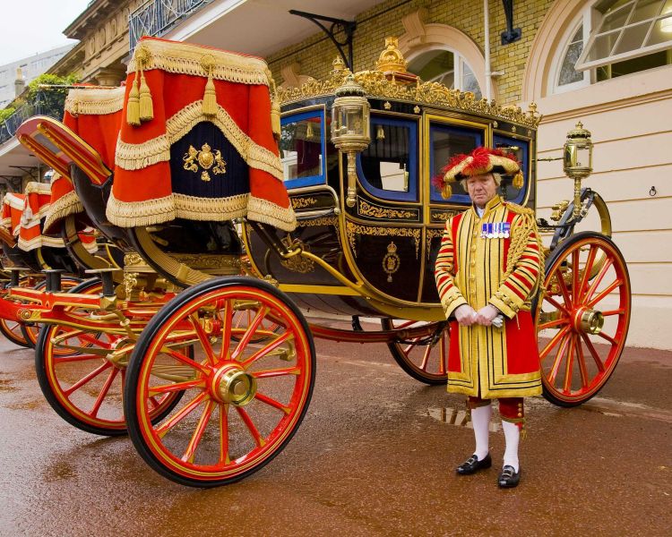 photo of a black and gold carriage decked out ready for ceremony with a man dressed in red and gold uniform standing next to it