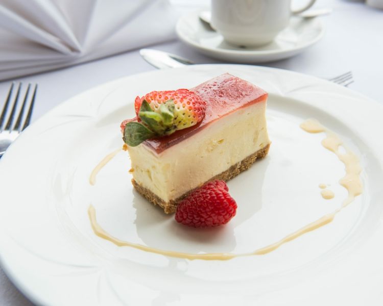 a slice of strawberry cheesecake on a white plate with a strawberry on the side