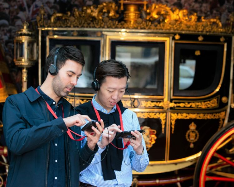 visitors listening to a multimedia guide at the royal mews museum standing in front of an ornate carriage