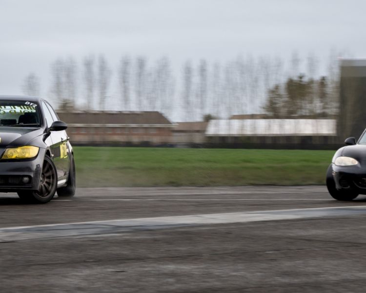 a black mx5 and black bmw side by side on a track as part of a drift battle experience