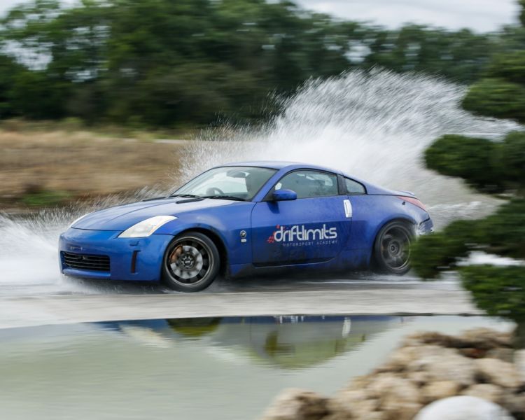 a blue sportscar driving through water on a track as part of a nissan and bmw drift battle experience day