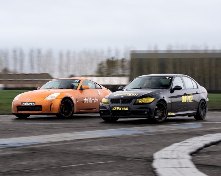 an orange nissan 350z sportcar and a black BMW sportscar side by side at a hemel hemstead race track as part of a drift battle driving experience