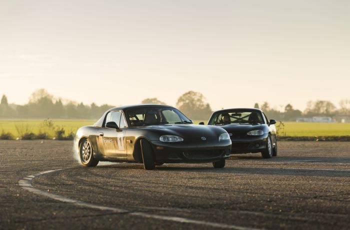 two black mx5 sports cars on a race track as part of a drifting experience