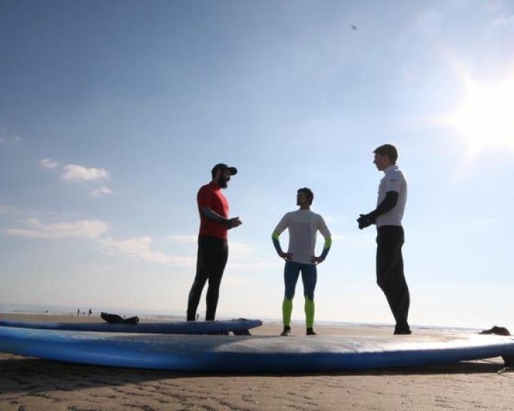 3 men standing on a beach beside surf boards