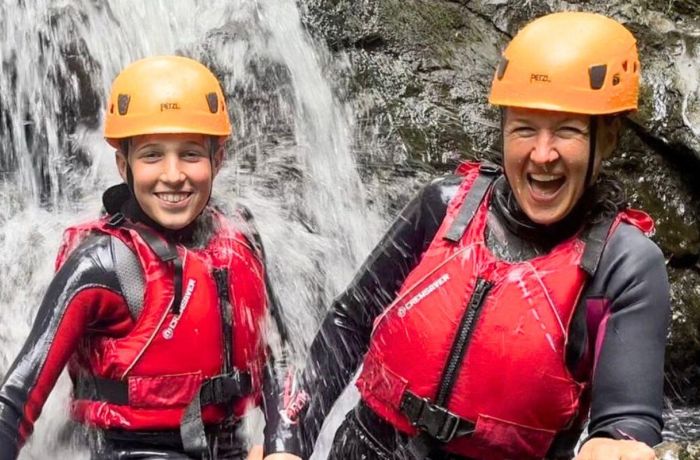 Young boy and woman standing in a waterfall