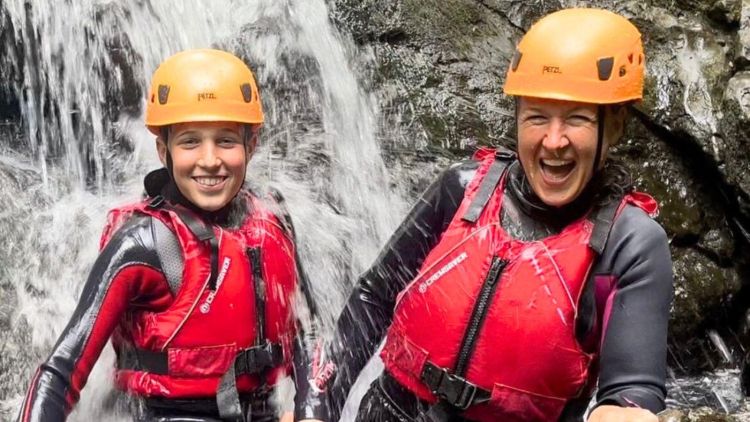 Young boy and woman standing in a waterfall
