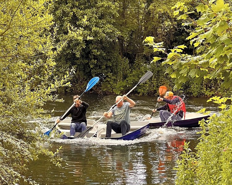 three people in row boats on the boating lake of a glamping site in cambridgeshire