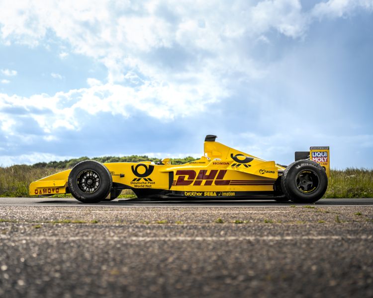 a side view of a yellow jordan formula one race car on a race track  against a cloudy sky background