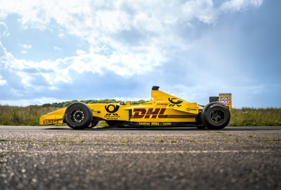 a side view of a yellow jordan formula one race car on a race track  against a cloudy sky background