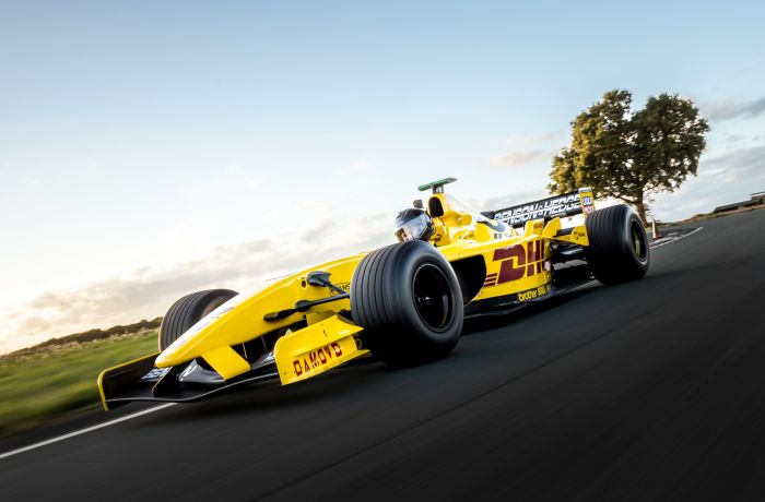 a yellow jordan f1 race car on a race track against a clear sky background