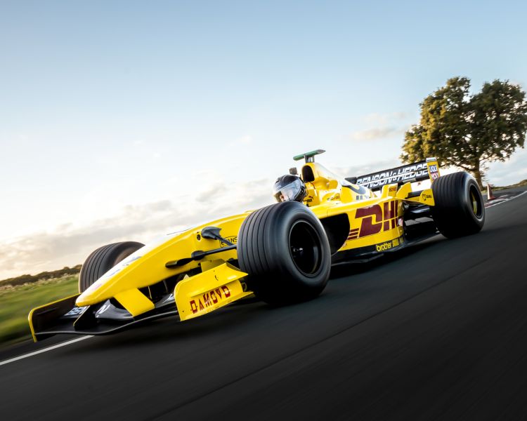 a yellow jordan f1 race car on a race track against a clear sky background