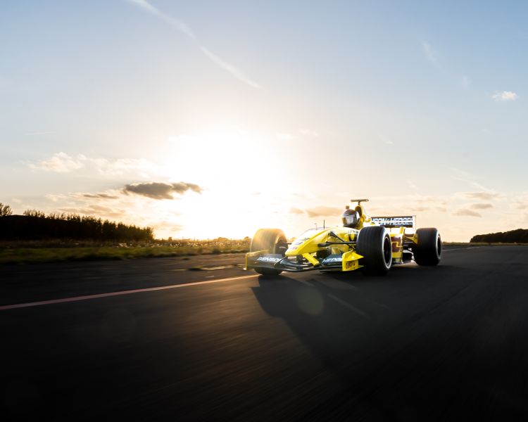 race car driving on a track with the sun setting behind it as part of a driving experience