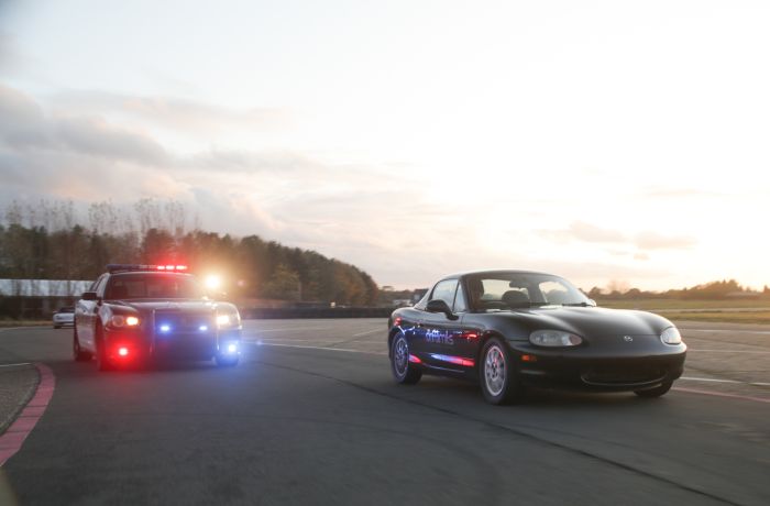 a police car with flashing lights chasing a black sports car on a race track as part of a police pursuit experience