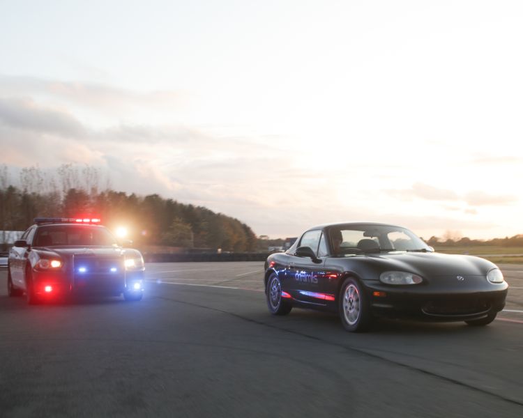 a police car with flashing lights chasing a black sports car on a race track as part of a police pursuit experience