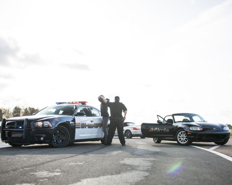 a police car and sports car side by side with a man being stopped by a policeman as part of a police pursuit experience