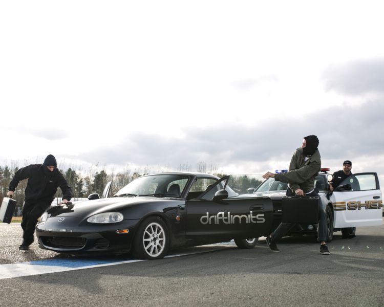 two people running out of a black sports car followed by a policeman getting out of a police car