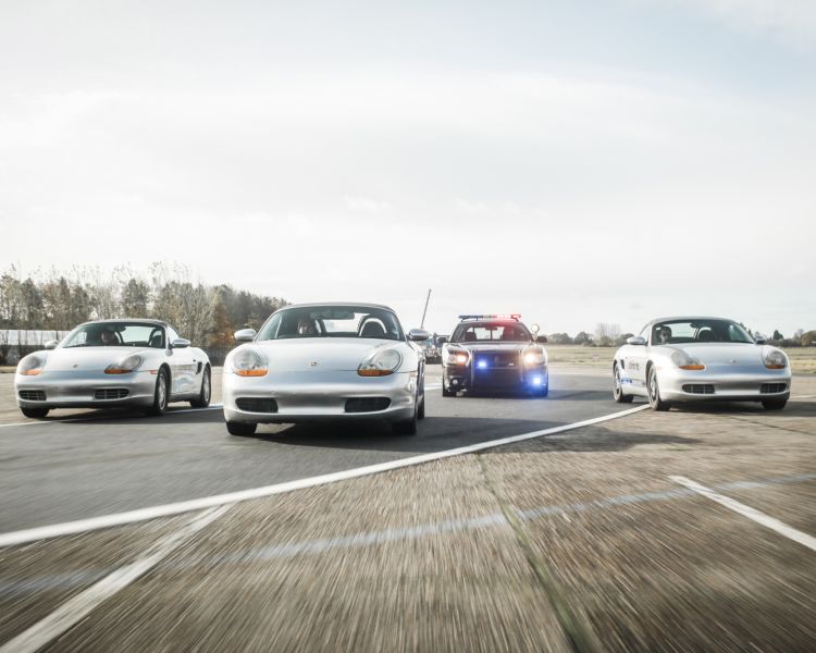 three sports cars and one police car side by side on a race track