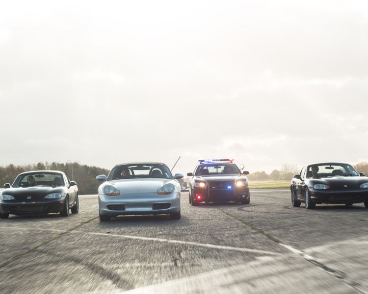 front view of four cars side by side on a race track, one of them is a police car