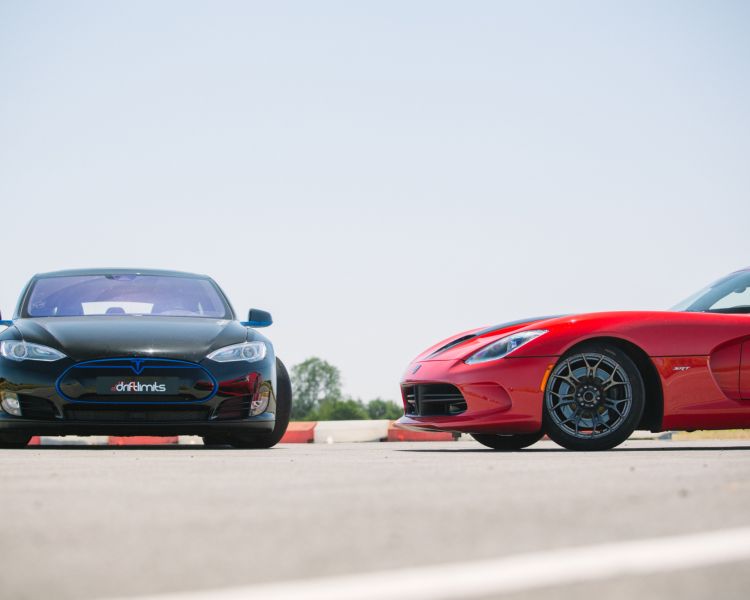 two supercars, a tesla and a viper, side by side on a race track.