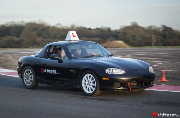 a young person learning how to drive a black supercar with an instructor on a racetrack
