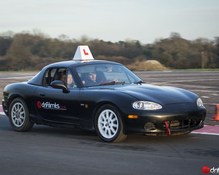 a young person learning how to drive a black supercar with an instructor on a racetrack