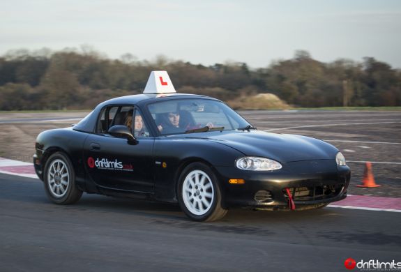 a young person learning how to drive a black supercar with an instructor on a racetrack