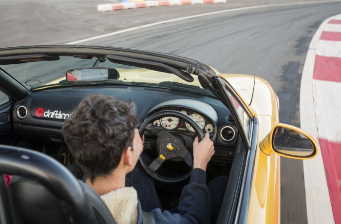 close up of a young person behind the wheel of a yellow supercar driving on a race track