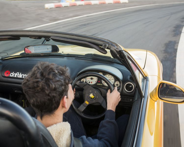 close up of a young person behind the wheel of a yellow supercar driving on a race track
