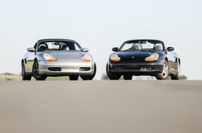front view of a silver porsche boxter next to a black porche boxter on a track
