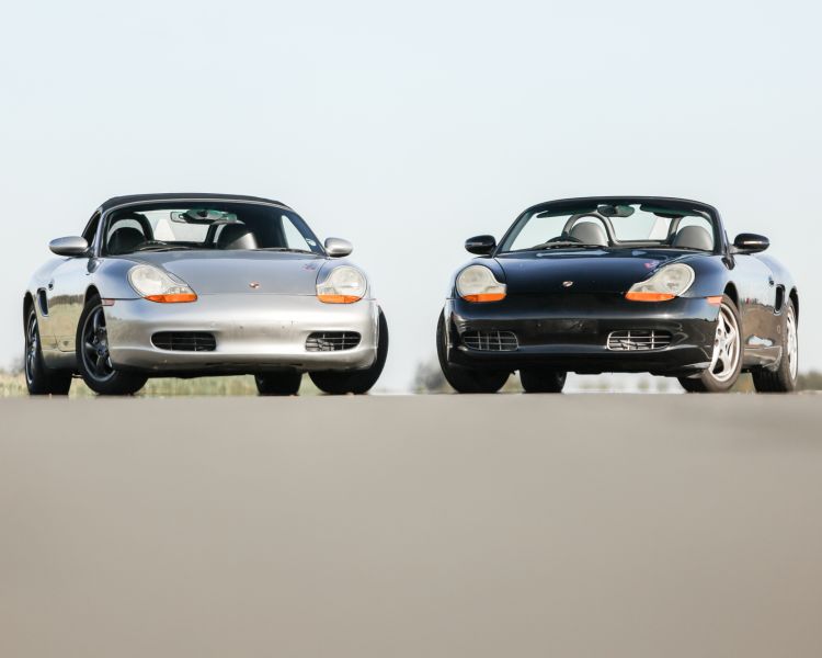 front view of a silver porsche boxter next to a black porche boxter on a track