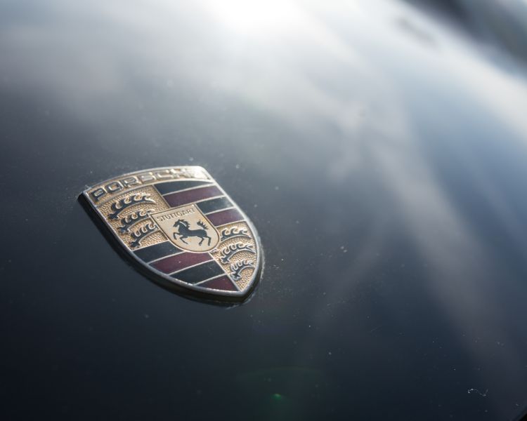 close up of the porche badge on the front of a black porsche boxter
