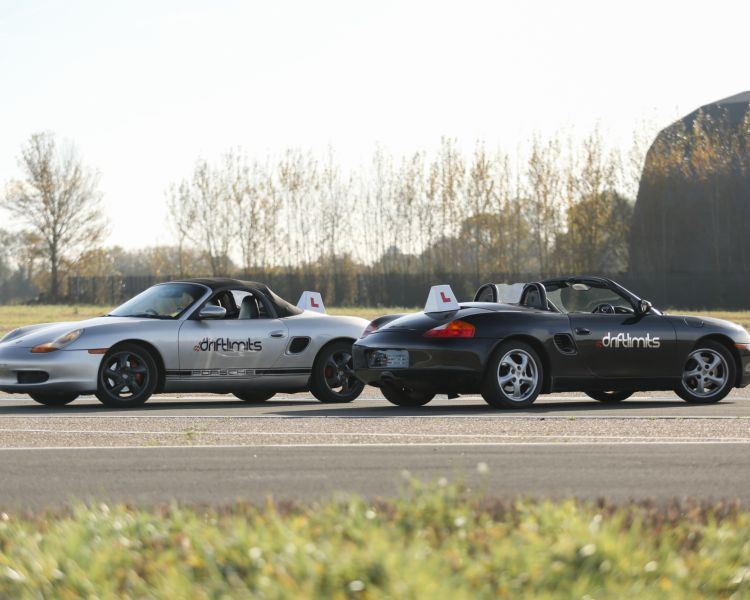 a silver porche boxter 5 and a black porche boxter side by side on a runway track