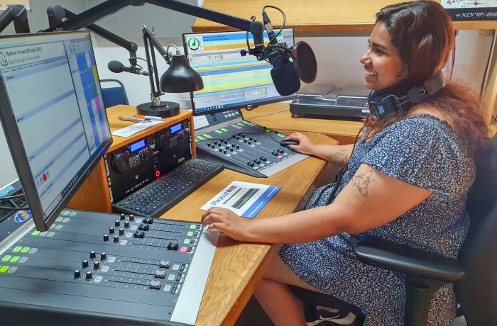 woman sat in front of a microphone at a radio station on a record your own show experience